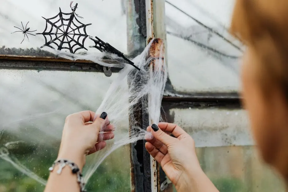 A close-up shot of a woman removing spider webs from a dirty window with her hands.